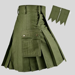 May include: An olive green utility kilt featuring a structured waistband with belt loops, deep vertical pleats, and a large cargo pocket on the front secured with two metallic snaps. Two matching olive green fabric tabs are positioned separately.