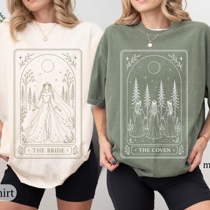 May include: Ivory and moss green t-shirts with tarot card-style graphics. The ivory shirt features "THE BRIDE" with a bride illustration. The moss green shirt displays "THE COVEN" with three figures. Both shirts have a "FULLY CUSTOMIZABLE" label.