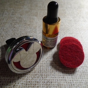 May include: A silver car air freshener with a Mickey Mouse silhouette and a red felt pad. A small bottle of Bergamot essential oil and three red felt pads are also shown.