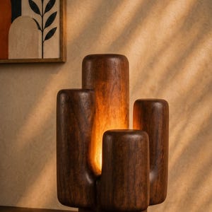 Op de afbeelding: Een donkerbruine houten tafellamp met een gladde, afgeronde, gelaagde structuur die lijkt op een cactus. De lamp heeft een centrale verticale opening die een warm, zacht schijnsel uitstraalt vanuit een interne lichtbron in het hout.