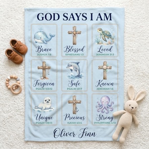 May include: A light blue baby blanket with the text "GOD SAYS I AM" and illustrated squares with inspirational words and Bible verses. The blanket features a whale, cross, turtle, dolphin, seal, and octopus. The name "Oliver Finn" is printed at the bottom.