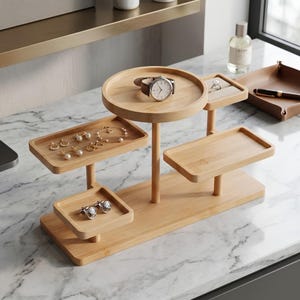 May include: A multi-tiered bamboo jewelry organizer featuring a circular top tray, two rectangular trays, and one square tray. The stand holds a wristwatch, a bracelet, several pairs of earrings, and a pair of cufflinks on its various levels.