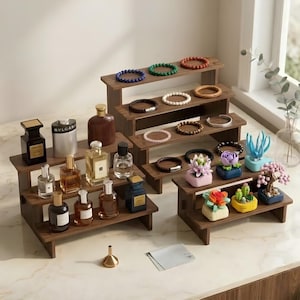 May include: Two tiered wooden display stands holding various glass perfume bottles, beaded bracelets, and small decorative succulent-shaped building block sets. A small metal funnel and a rectangular cleaning cloth are placed in the foreground.