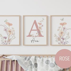 May include: Three framed floral art prints. The prints feature watercolor flowers in peach, pink, and lavender hues, with a butterfly accent. The center print displays the letter "A" in pink, with the name "Ava" below.