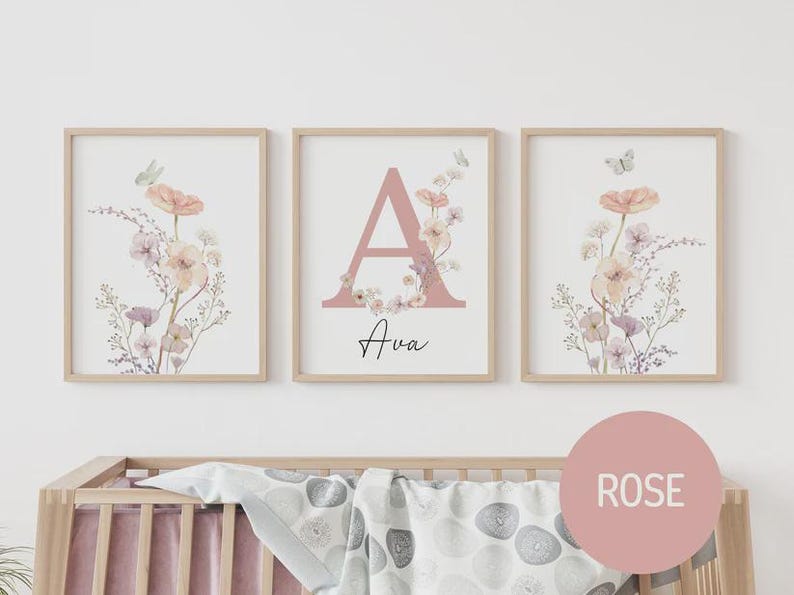 May include: Three framed floral art prints. The prints feature watercolor flowers in peach, pink, and lavender hues, with a butterfly accent. The center print displays the letter "A" in pink, with the name "Ava" below.