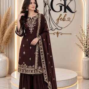 Könnte beinhalten: Ein dunkelbraunes dreiteiliges Set bestehend aus einer knielangen Tunika mit goldener Stickerei am Ausschnitt und Saum, kombiniert mit einer weiten Hose und einem passenden Dupatta, beide mit aufwendigen goldenen Blumenmustern.