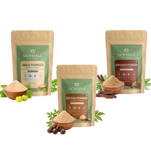 Puede incluir: Tres bolsas de polvos Mohana Wellness: Amla, Reetha y Shikakai. Cada bolsa es de color beige con una etiqueta verde. Los polvos se muestran en cuencos de madera con hojas y frutas. El polvo de Amla va acompañado de frutos verdes.