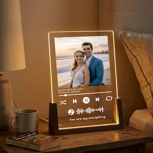 May include: A personalized LED night light featuring a couple's photo. The clear acrylic panel displays a photo, song title, artist, and the text "You are my everything." The light sits in a dark wooden base, emitting a warm glow.