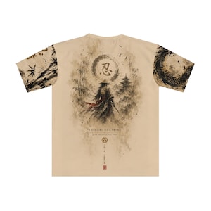 May include: A beige t-shirt featuring a dark ink-wash style graphic on the back. The design depicts a figure in a conical hat, bamboo, a pagoda, and a circular symbol with Japanese text. The sleeves have black patterns, and the text reads SHINOBI DOCTRINE.