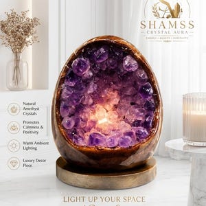 May include: A decorative amethyst crystal lamp with a warm ambient glow. The lamp features a wooden base and a geode-like structure filled with purple crystals. The text on the lamp says "LIGHT UP YOUR SPACE with Positive Energy."