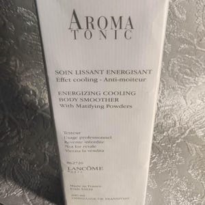Könnte beinhalten: Weiße rechteckige Schachtel mit Lancôme Aroma Tonic Body Smoother. Die Schachtel enthält den Produktnamen und die Beschreibung in Englisch und Französisch. Das Produkt ist ein kühlender Body Smoother mit mattierenden Pudern. Die Schachtel ist als Tester gekennzeichnet.