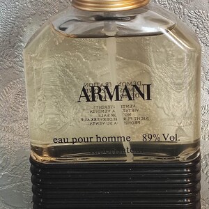 Könnte beinhalten: Rechteckiger Parfümflakon mit schwarzem Deckel und goldenen Akzenten. Die Flasche enthält eine klare Flüssigkeit und trägt den Markennamen "ARMANI". Der Text "eau pour homme" und "89% Vol." sind ebenfalls aufgedruckt.