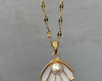 May include: A gold chain necklace with a white seashell pendant featuring a pearl in the center.