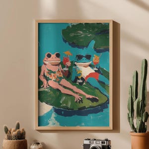 May include: A framed art print depicts two anthropomorphic frogs lounging on lily pads, enjoying cocktails. One frog wears sunglasses and swim trunks, the other a floral swimsuit. The background is a turquoise pond with green lily pads.