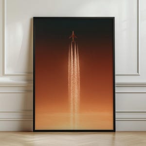 Pode incluir: Uma impressão de arte de parede vertical emoldurada apresentando a silhueta de um avião voando para cima contra um céu degradê que transita de cinza carvão escuro no topo para um laranja quente e brilhante na base, com dois rastros brancos.