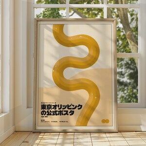 Puede incluir: Un póster rectangular enmarcado que presenta una gran línea ondulada de color amarillo mostaza centrada sobre un fondo crema. La esquina inferior izquierda muestra texto japonés en negro y la esquina inferior derecha tiene dos círculos pequeños.