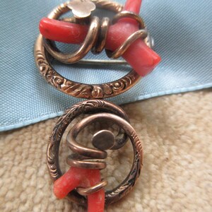 Puede incluir: Un broche vintage con dos piezas de coral engastadas en un marco de metal dorado. El coral es de un color rojo vibrante y el marco est&aacute; finamente grabado con dise&ntilde;os florales.