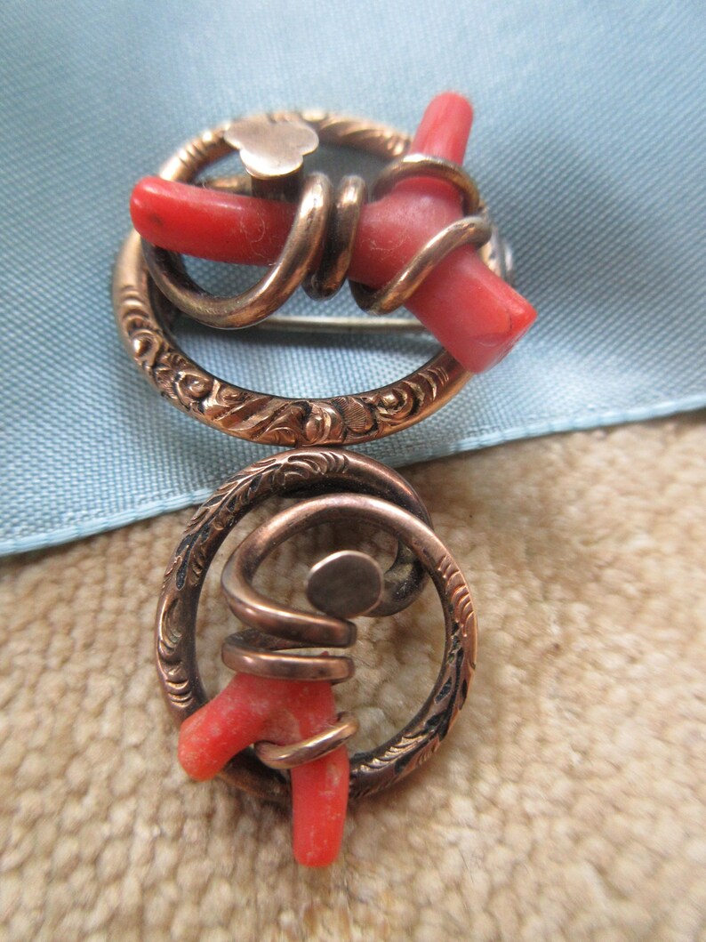 Puede incluir: Un broche vintage con dos piezas de coral engastadas en un marco de metal dorado. El coral es de un color rojo vibrante y el marco est&aacute; finamente grabado con dise&ntilde;os florales.