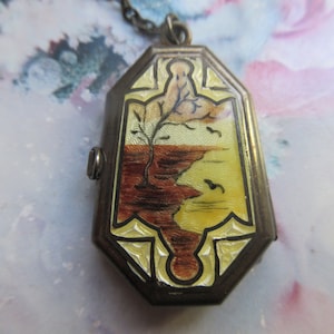 May include: A silver locket with a chain, featuring an enamel painted scene of a tree and a body of water. The enamel is in shades of brown, yellow, and white.