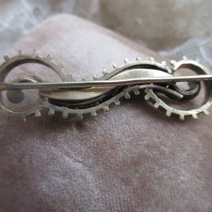 May include: Silver tone brooch with a swirling design and a pin closure on the back.