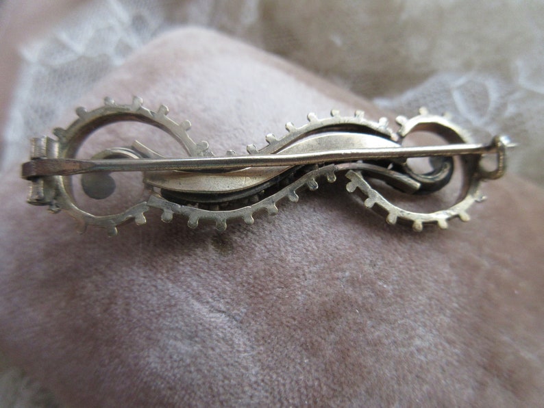 May include: Silver tone brooch with a swirling design and a pin closure on the back.