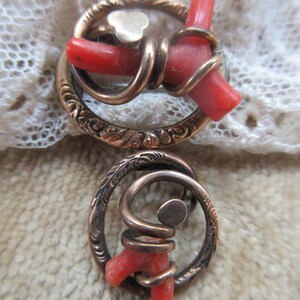 Puede incluir: Un par de pendientes antiguos con un dise&ntilde;o circular. Los pendientes est&aacute;n hechos de metal dorado y presentan una pieza de coral rojo envuelta en espiral. El metal est&aacute; grabado con un patr&oacute;n floral.