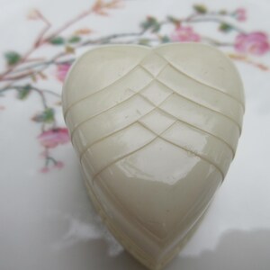 May include: A heart-shaped, off-white decorative object with a textured, layered design. The object is set against a backdrop of a white surface with a floral pattern in pink and green.