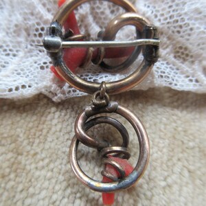 Puede incluir: Un broche vintage con un dise&ntilde;o circular que presenta una pieza de coral rojo retorcida y un dije colgante con un dise&ntilde;o similar.