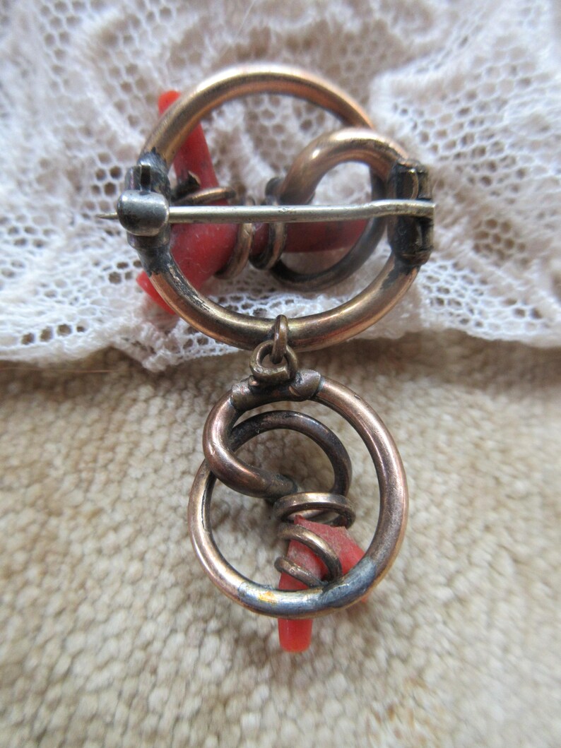 Puede incluir: Un broche vintage con un dise&ntilde;o circular que presenta una pieza de coral rojo retorcida y un dije colgante con un dise&ntilde;o similar.
