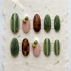 May include: A set of ten press-on nails featuring various designs including olive green vertical stripes with gold star accents, nude bases with 3D green olives, glossy brown tortoiseshell patterns, and deep green nails with carved leaf textures.