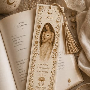 Peut inclure: Marque-page beige avec un pompon, représentant une illustration d'une femme aux longs cheveux et le mot "LOVE" en haut. Le marque-page porte l'inscription "Je suis forte, je suis puissante, je suis digne."