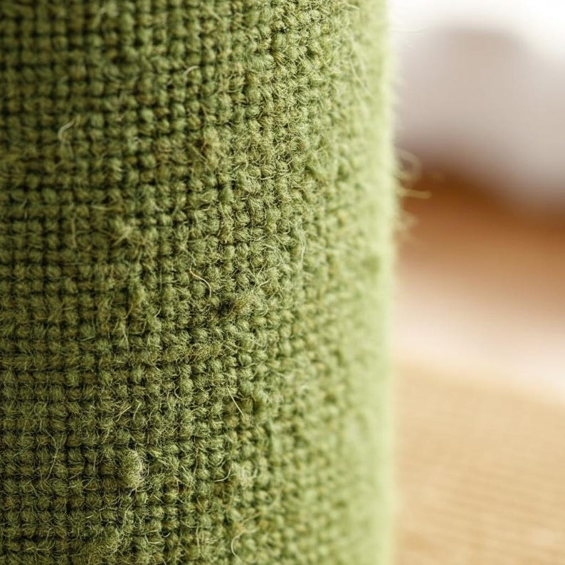 Peut inclure: Gros plan sur un objet cylindrique recouvert d'un tissu vert olive textur&eacute;. Le tissu a un aspect tiss&eacute; avec des fibres visibles et une texture l&eacute;g&egrave;rement floue. L'arri&egrave;re-plan est flou, avec des tons neutres.