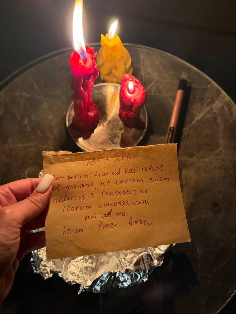 A hand holding a handwritten note with a candlelit candle and a pen on a table.