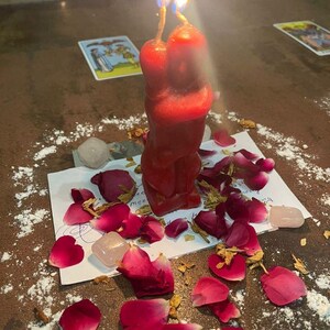 A red candle with a flame burning on a table, surrounded by rose petals and crystals, creating a romantic and spiritual atmosphere.