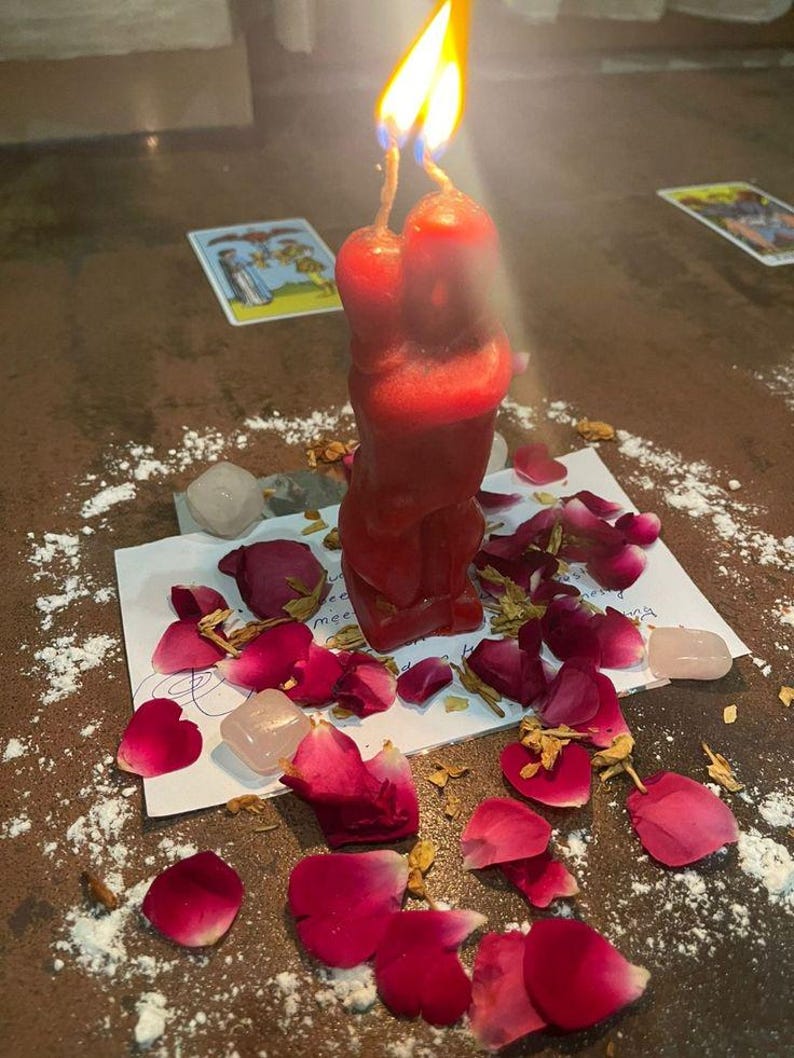 A red candle with a flame burning on a table, surrounded by rose petals and crystals, creating a romantic and spiritual atmosphere.