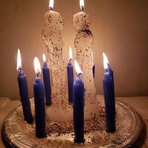 A silver tray holds nine lit candles in various sizes, arranged in a circular pattern.
