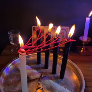a silver tray with a white candle and a pair of scissors, surrounded by lit candles and a glass of water on a dark wooden table.