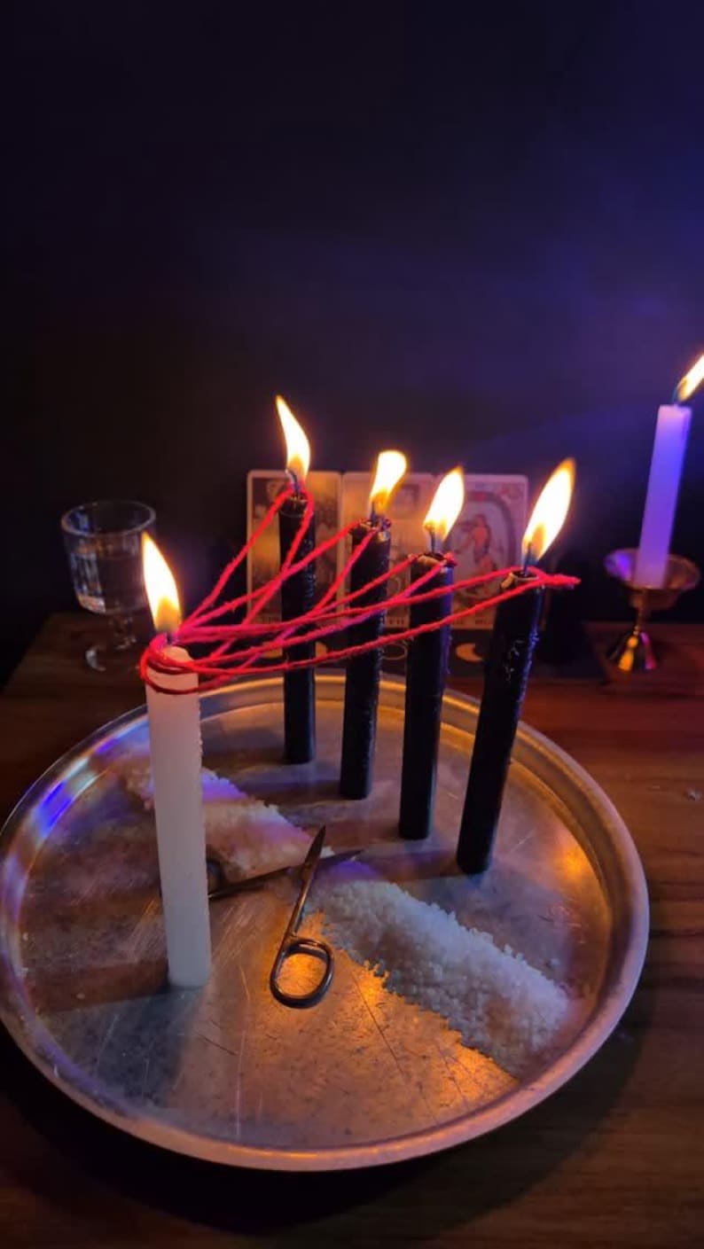 a silver tray with a white candle and a pair of scissors, surrounded by lit candles and a glass of water on a dark wooden table.