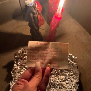 A hand holding a piece of paper with handwritten text, with two lit candles in the background.