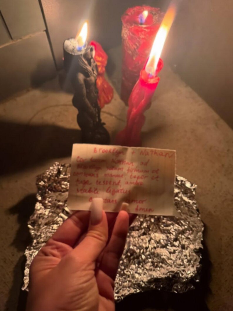 A hand holding a piece of paper with handwritten text, with two lit candles in the background.
