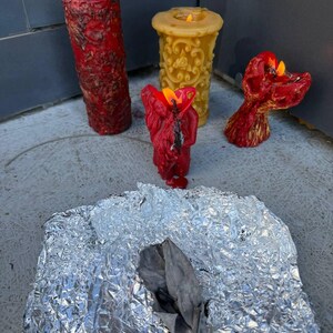 three candles in various stages of burning, with one candle having melted and two others still burning. The candles are placed on a piece of aluminum foil, and there is a crumpled piece of aluminum foil in the foreground.