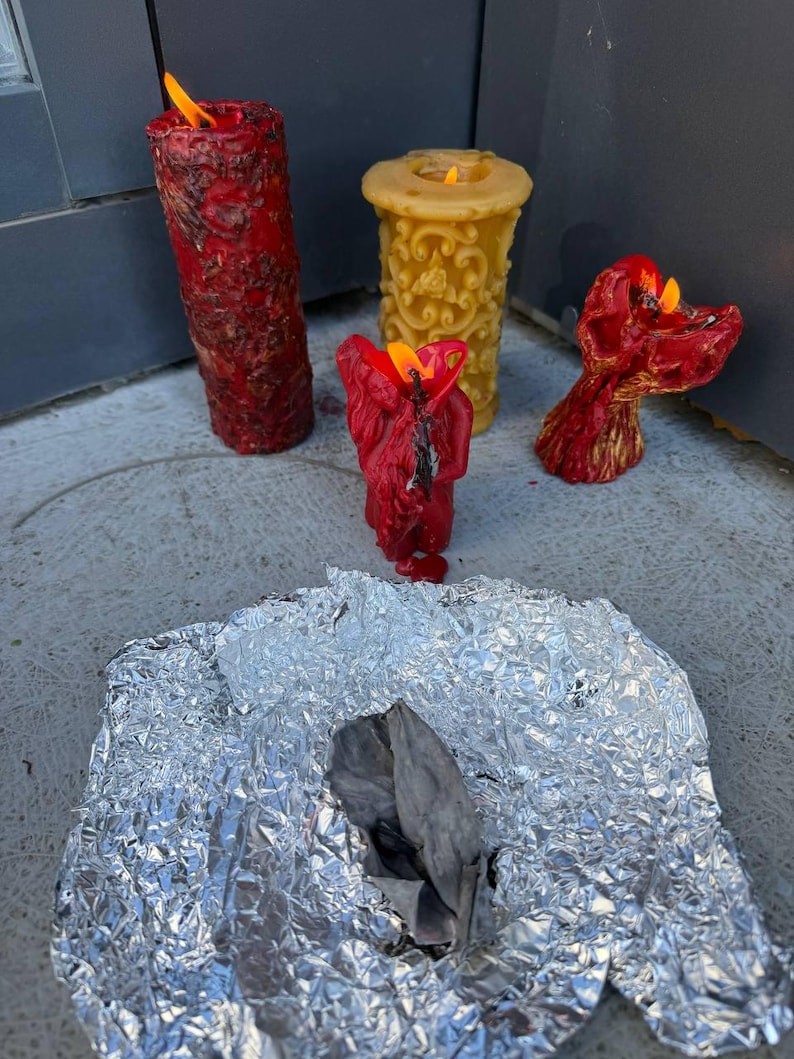 three candles in various stages of burning, with one candle having melted and two others still burning. The candles are placed on a piece of aluminum foil, and there is a crumpled piece of aluminum foil in the foreground.