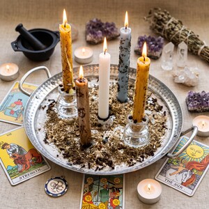 a silver tray with five candles, surrounded by tarot cards, crystals, and other mystical objects, creating an atmosphere of spiritual exploration and ritual.