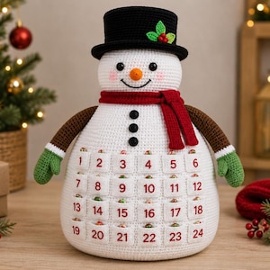 May include: A white crocheted snowman advent calendar featuring a black top hat with holly, a red scarf, brown arms with green mittens, and three black buttons. The body has twenty-four small white pockets numbered one through twenty-four in red.