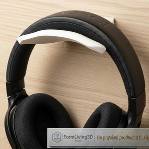Könnte beinhalten: Ein weißer Wandhalter für Kopfhörer, an dem ein schwarzer Over-Ear-Kopfhörer hängt. Der Halter hat ein geschwungenes Design zur Unterstützung des Kopfbügels. Ein kleines rechteckiges Etikett unten zeigt FormLiving3D No physical product, STL File.