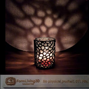 Könnte beinhalten: Ein dekorativer Kerzenhalter mit schwarzem, durchbrochenem Design. Der zylindrische Kerzenhalter steht auf einer Holzoberfläche. Das Licht der Kerze wirft ein Muster auf den Hintergrund. Der Text "FormLiving3D CHARACTER" ist sichtbar. Der Kerzenhalter ist ca. 10 cm hoch.