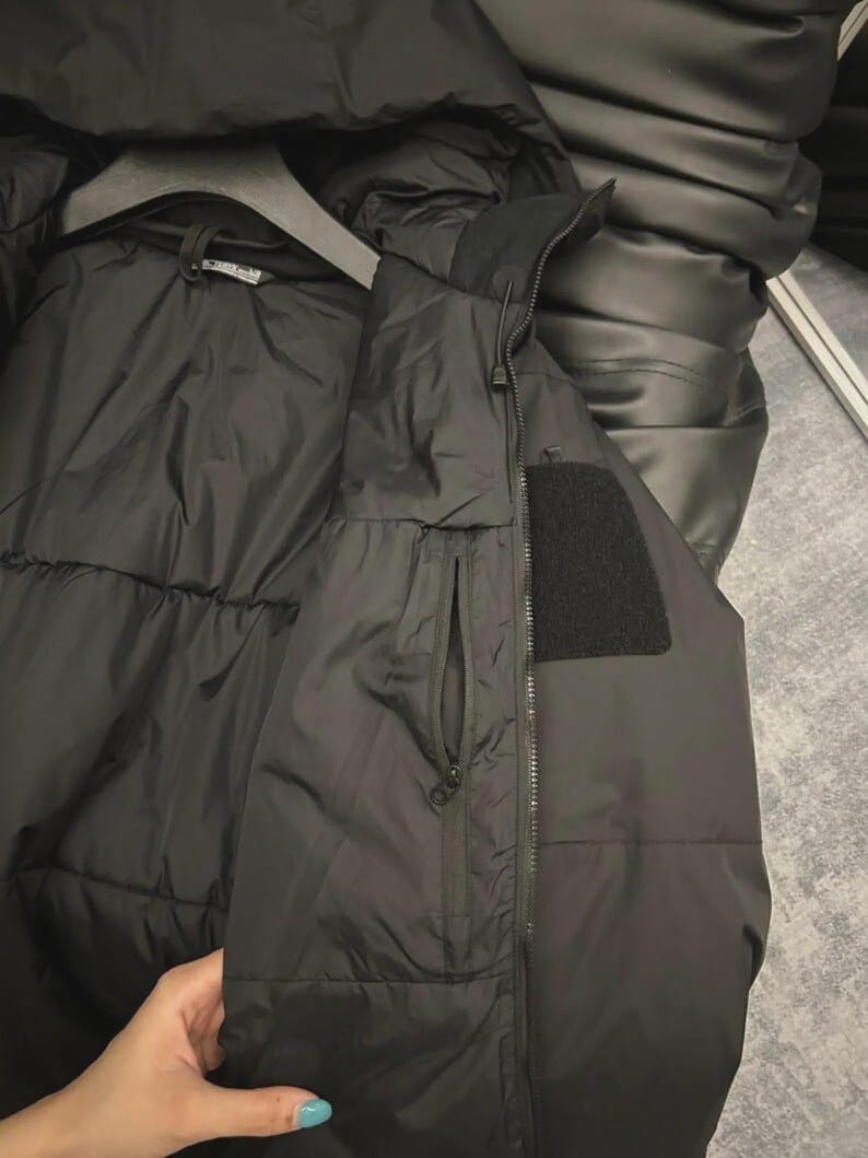 May include: Black puffer jacket and vest set. The jacket has a hood and is hanging on a hanger. The vest has a zip closure and a small pocket. The vest also has a black patch.