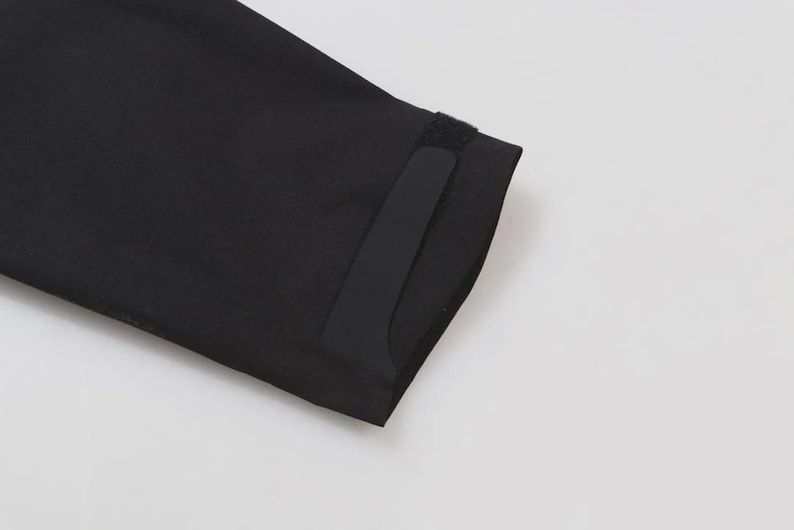 May include: Close-up of a black fabric sleeve with a velcro closure. The sleeve is angled, showing the edge and a portion of the cuff. The background is plain white.