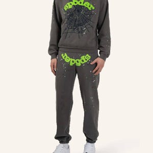 May include: A gray sweatsuit with the word "spider" in green, and a spiderweb graphic on the sweatshirt. The sweatpants and sweatshirt have a speckled design. The person is wearing white sneakers.