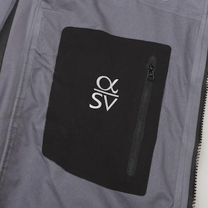 May include: Close-up of the interior of a gray jacket. A black pocket with a zipper is visible, featuring the white letters "&alpha;SV". The jacket's interior is a light gray color.
